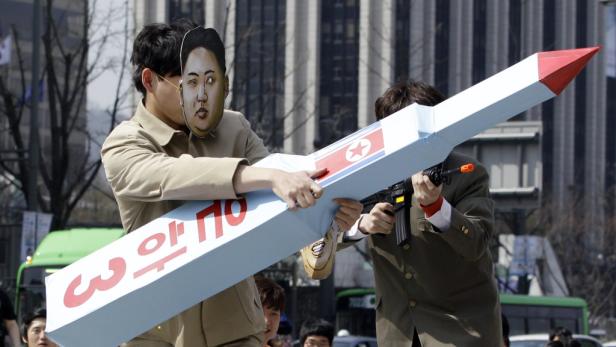 Zwei Männer demonstrieren mit einer Raketenattrappe und einer Kim-Jong-Un-Maske.