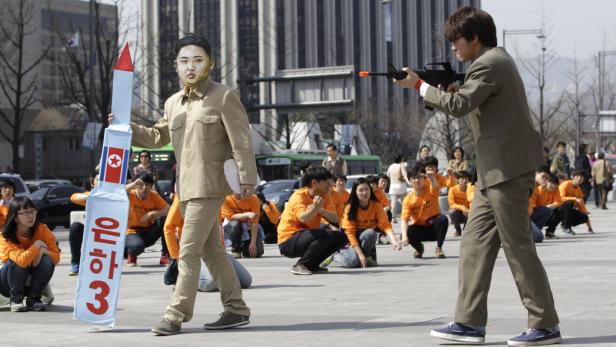 Ein Mann mit Kim-Jong-Un-Maske hält eine Raketenattrappe, während ein anderer mit einer Spielzeugwaffe zielt.