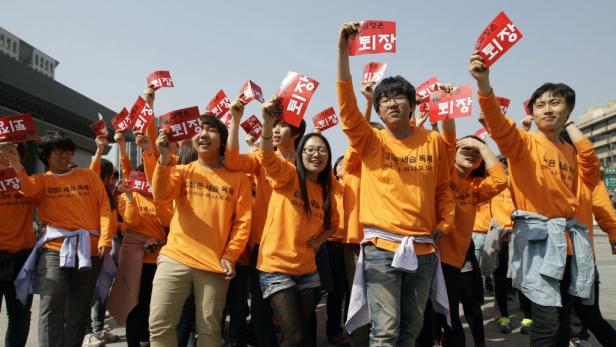 Eine Gruppe junger Menschen demonstriert mit roten Schildern und orangefarbenen T-Shirts.