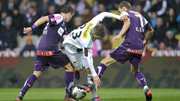 Zwei Fußballspieler in lila Trikots kämpfen um den Ball mit einem Spieler in Weiß.