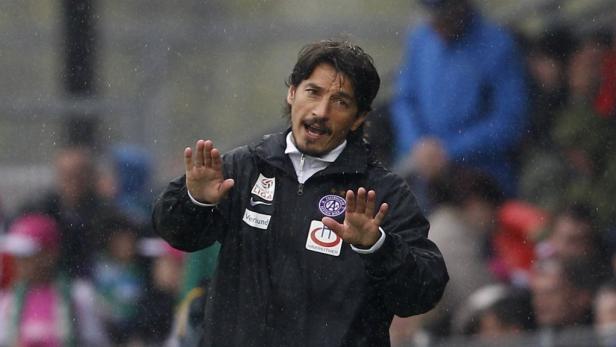 Ein Fußballtrainer gestikuliert während eines Spiels im Regen.