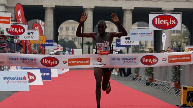 Ein Läufer überquert mit erhobenen Armen die Ziellinie eines Marathons.