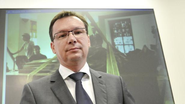 Ein Mann mit Brille und Anzug steht vor einer Leinwand mit einer Filmszene.