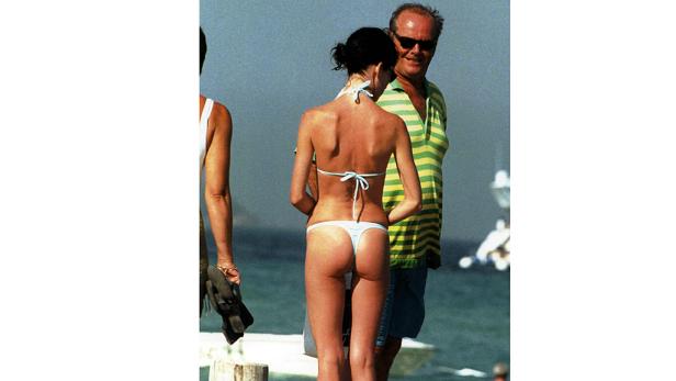 Eine Frau im Bikini steht am Strand, während Jack Nicholson im Hintergrund steht.