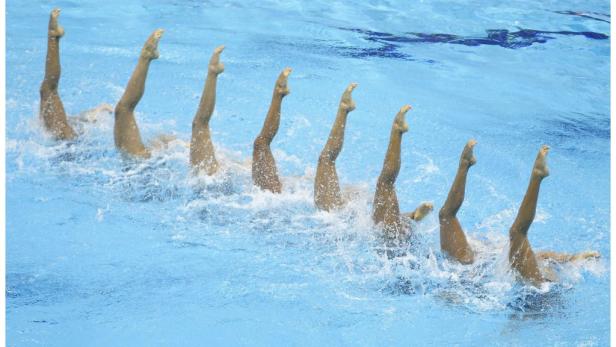 Mehrere Synchronschwimmerinnen zeigen ihre Beine aus dem Wasser.