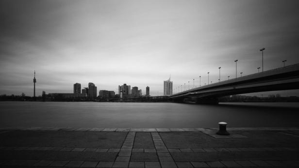 Eine Schwarzweißaufnahme von Wien mit der Donau, einer Brücke und der Skyline.