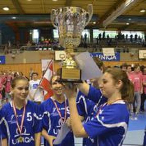 Ein Team junger Frauen hält einen großen goldenen Pokal in die Höhe.