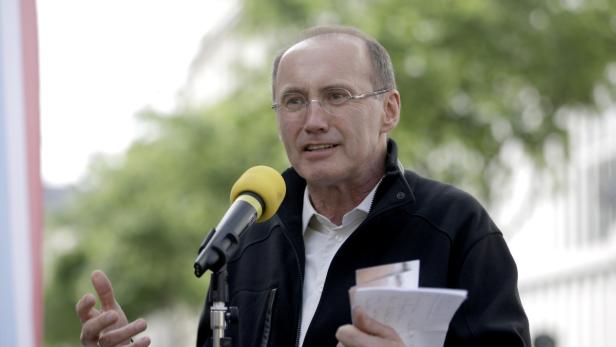 Ein Mann mit Brille spricht in ein gelbes Mikrofon und hält Notizen in der Hand.