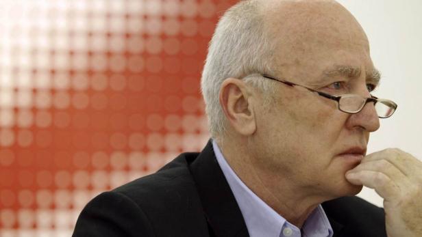 Ein Mann mit Brille und Anzug hält seine Hand ans Kinn.