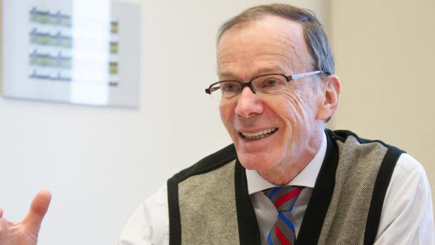 Ein lächelnder älterer Mann mit Brille und Krawatte gestikuliert.