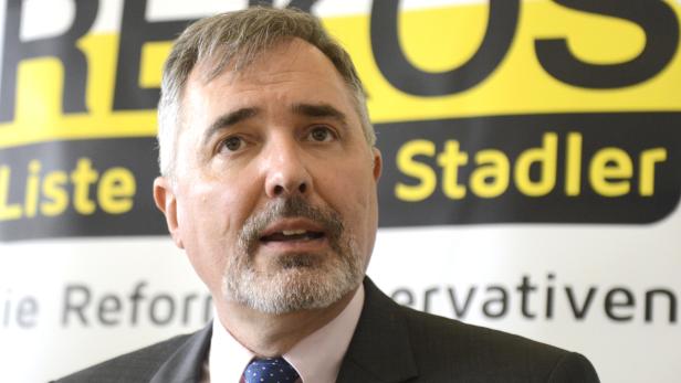 Ein Mann mit Bart steht vor einem Banner mit der Aufschrift „Liste Stadler“.