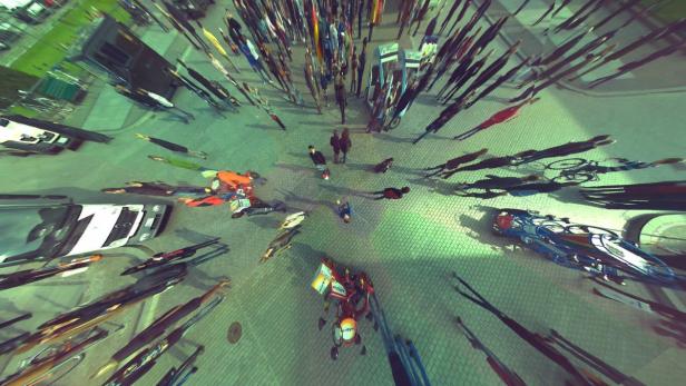 Eine Menschenmenge und verschiedene Fahrzeuge sind aus der Vogelperspektive auf einer gepflasterten Fläche zu sehen.