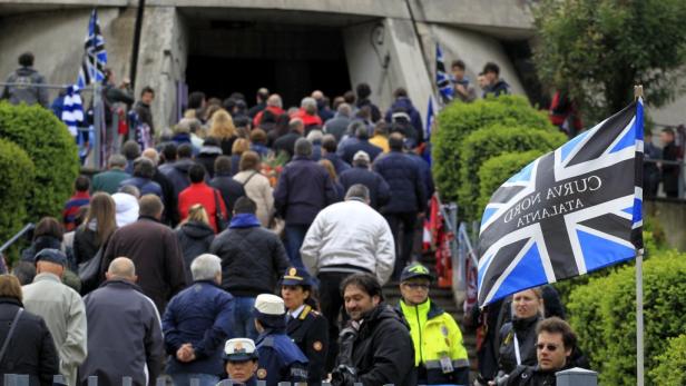 Eine Menschenmenge betritt ein Gebäude, im Vordergrund eine Flagge mit der Aufschrift „Curva Nord Atalanta“.