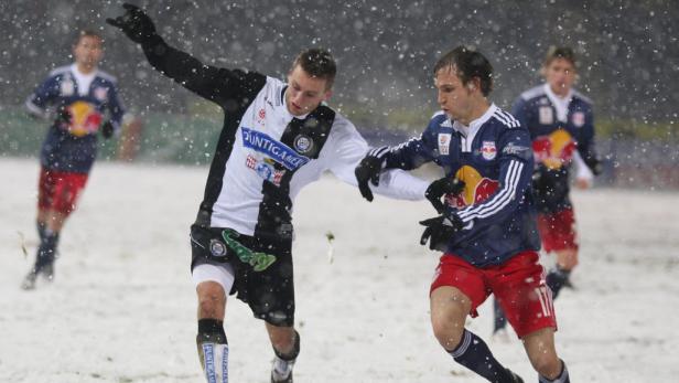 Zwei Fußballspieler kämpfen in einem Schneesturm um den Ball.