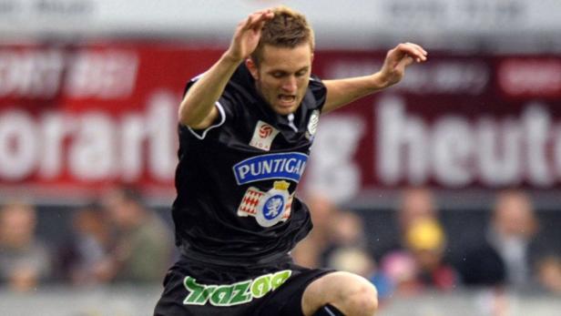 Ein Fußballspieler in einem schwarzen Trikot springt in die Luft.