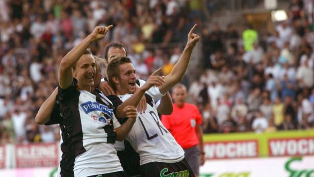 Jubelnde Fußballspieler feiern auf dem Rasen vor einer Zuschauermenge.