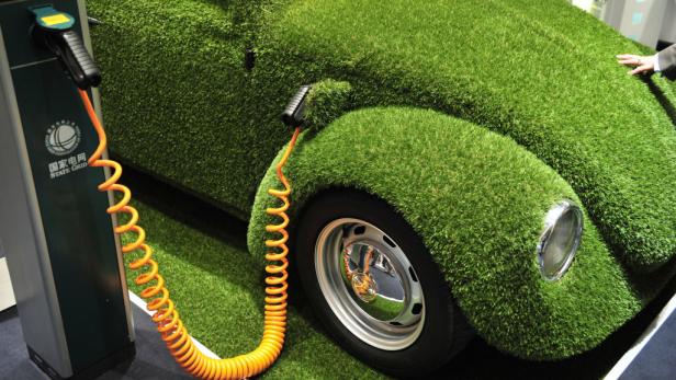 Ein mit Gras bedeckter VW Käfer wird an einer Ladestation aufgeladen.