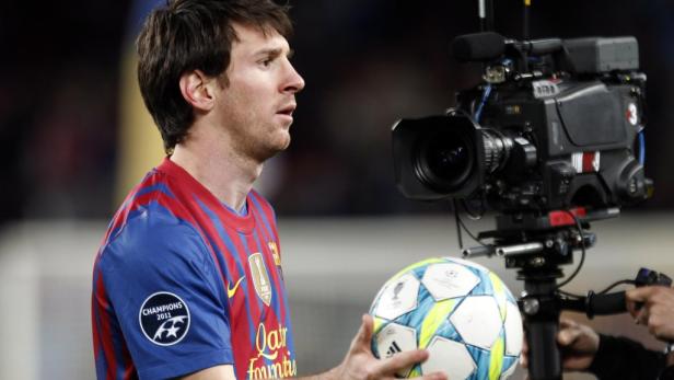 Lionel Messi hält einen Fußball vor einer Fernsehkamera.