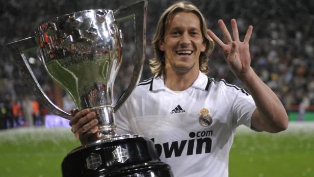 Ein lächelnder Fußballspieler von Real Madrid hält eine Trophäe und zeigt vier Finger.