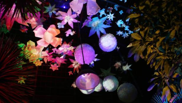 Dekorative Blumen und Kugeln hängen von der Decke, beleuchtet in verschiedenen Farben.