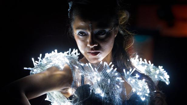 Eine Frau trägt ein futuristisches Kleid, das mit leuchtenden LED-Lichtern verziert ist.