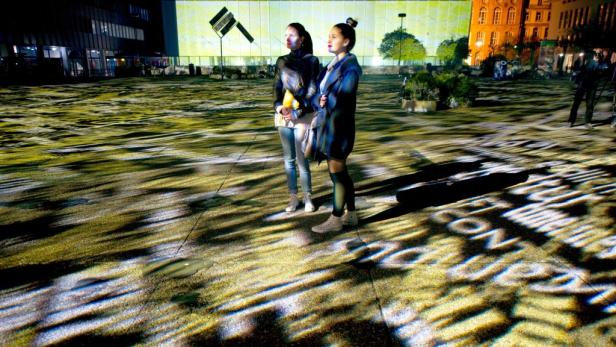 Zwei Frauen stehen auf einem Platz mit Lichtprojektionen in einer Stadt.