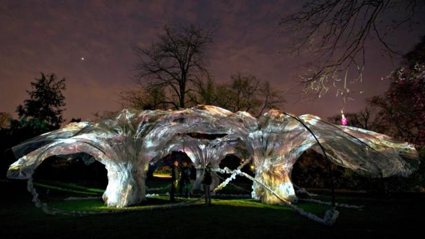 Eine beleuchtete Installation im Freien, die an eine Höhle oder einen Baum erinnert, mit Personen im Inneren.