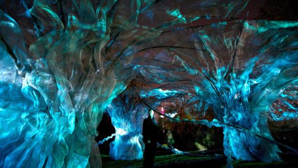 Eine Person steht unter einer Installation aus blau beleuchteten, transparenten Stoffen.