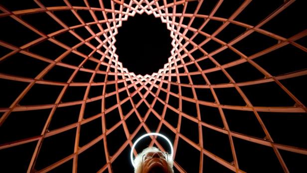 Ein Mann blickt in eine Kuppel aus Holzstreben mit einem leuchtenden Heiligenschein über seinem Kopf.