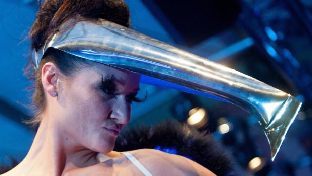 Eine Frau trägt eine futuristische, silberne Kopfbedeckung und falsche Wimpern.