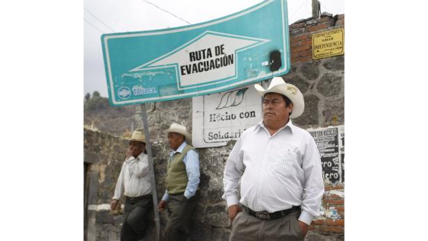 Drei Männer mit Hüten stehen unter einem Schild mit der Aufschrift „Ruta de Evacuación“.