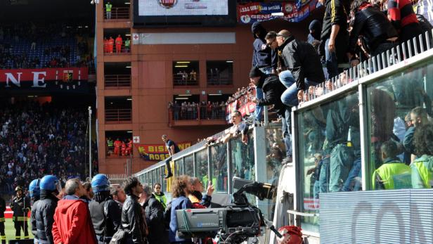 Fußballfans klettern auf eine Tribüne, während Sicherheitskräfte zusehen.