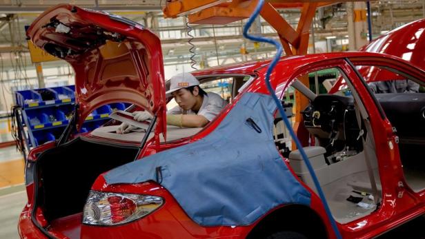 Ein Arbeiter montiert in einer Fabrik ein rotes Auto.