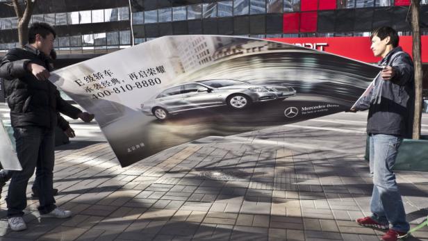 Zwei Männer halten ein Werbeplakat für eine Mercedes-Benz E-Klasse.