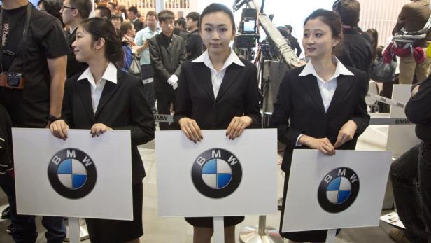 Drei Frauen in Anzügen präsentieren Schilder mit dem BMW-Logo auf einer Veranstaltung.