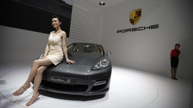Eine Frau posiert auf einem grauen Porsche Turbo S vor dem Porsche-Logo.