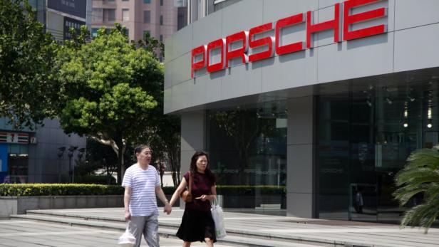 Ein Paar geht Händchen haltend vor einem Porsche-Autohaus entlang.