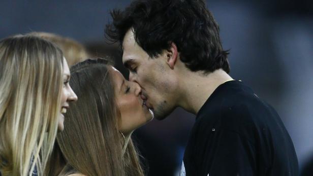 Ein Paar küsst sich, während eine Frau im Hintergrund lächelt.