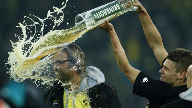 Ein Mann schüttet einem anderen eine Flasche „Brinkhoff's“ Bier über den Kopf.