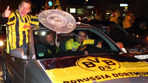 Fans von Borussia Dortmund feiern in einem Auto mit der Meisterschale.