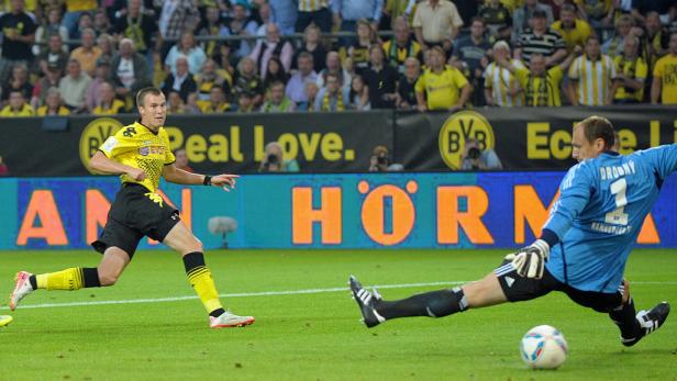 Ein Fußballspieler schießt auf das Tor, während der Torwart versucht, den Ball abzuwehren.