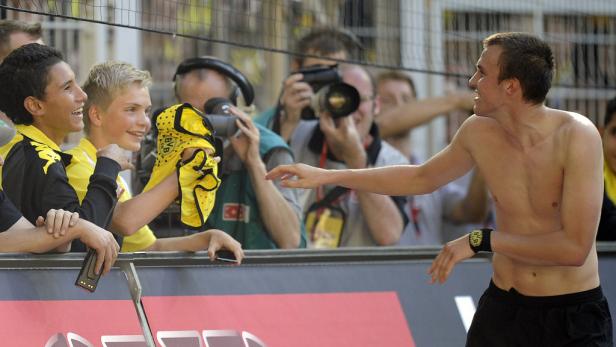 Ein barfüßiger Fußballspieler interagiert mit Fans hinter einer Absperrung.