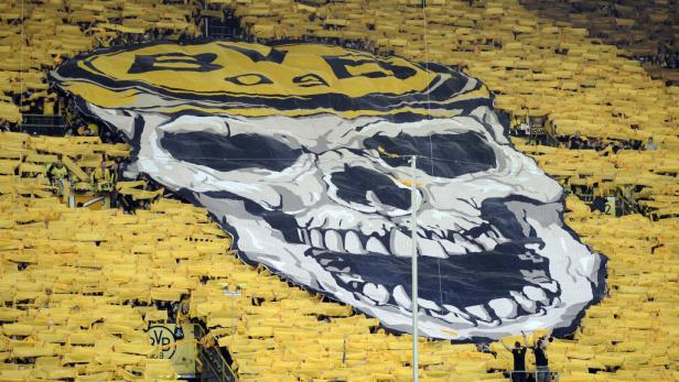 Eine Tribüne voller Borussia Dortmund Fans mit gelben Fahnen und einem riesigen Totenkopf-Banner.