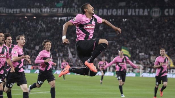 Ein Fußballspieler in pinkfarbenem Trikot springt jubelnd auf dem Spielfeld.