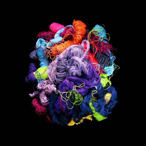 Ein Haufen bunter Wollknäuel liegt auf einem schwarzen Hintergrund.