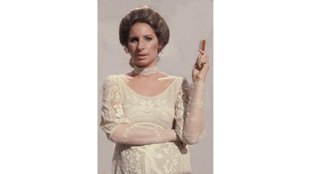 Barbra Streisand in einem weißen Spitzenkleid mit einem Gegenstand in der Hand.