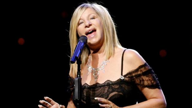 Barbra Streisand singt in einem schwarzen Kleid mit Spitze und einer Halskette vor einem Mikrofon.