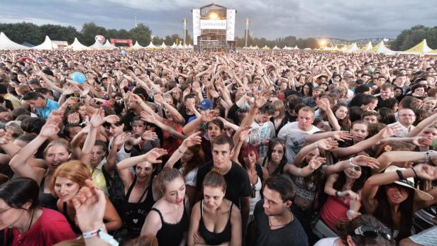 Eine große Menschenmenge jubelt auf einem Musikfestival vor einer Bühne.