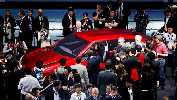 Ein rotes Auto wird auf einer Automesse von einer Menschenmenge umringt.
