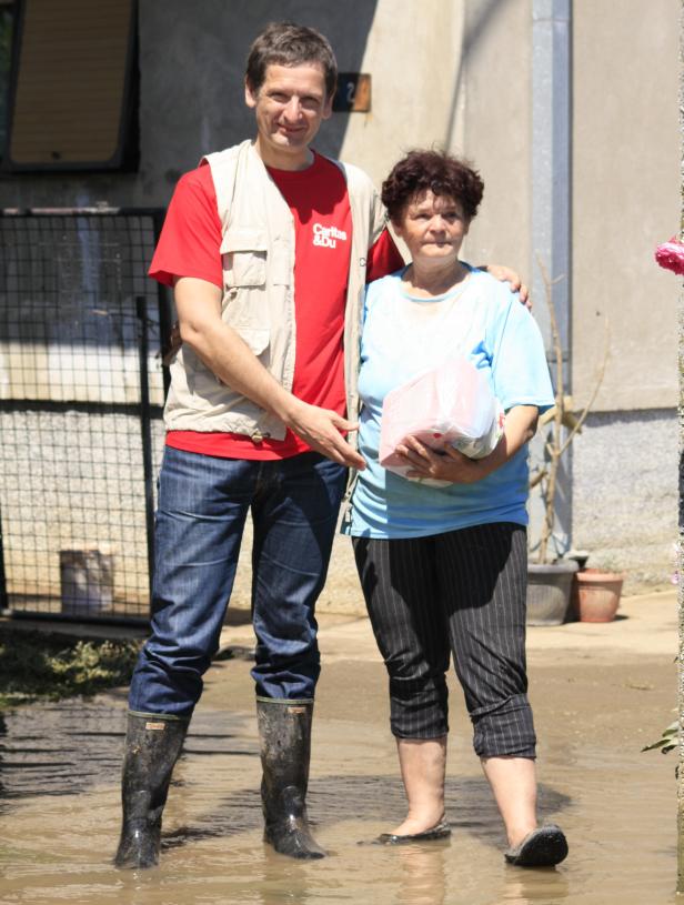 Ein Mann von Caritas steht mit einer älteren Frau im Hochwasser.